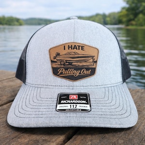 May include: Gray trucker hat with a black mesh back and a patch that reads "I Hate Pulling Out" with a boat graphic. The hat has a curved brim and an adjustable strap.