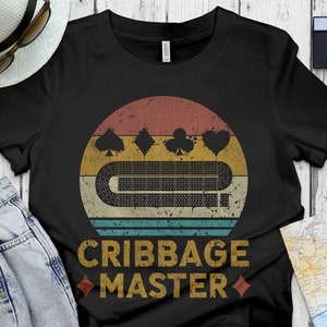 May include: Black t-shirt with a vintage-style illustration of a cribbage board and cards. The text "Cribbage Master" is printed in white below the illustration.