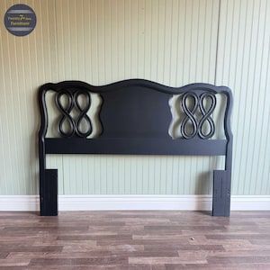 May include: Black wooden headboard with a curved top and decorative infinity symbol design. The headboard has two vertical supports and is painted black. The headboard is a furniture item.