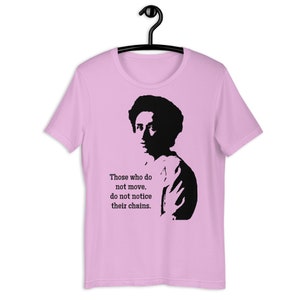 May include: Pink t-shirt featuring a black silhouette of a person and the quote "Those who do not move, do not notice their chains."