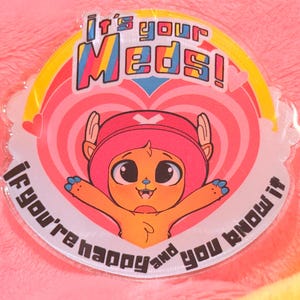 May include: A clear sticker with a cartoon character in a pink hat and the text "It's your Meds! If you're happy and you know it". The character is orange with blue accents and is set against a pink heart.