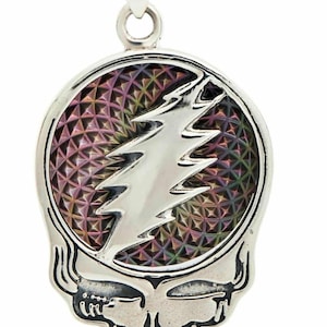 May include: A silver pendant featuring a stylized skull design with a lightning bolt emblem. The pendant has a colorful, geometric patterned background. The skull has a detailed, etched design. The pendant is likely made of metal and is designed to be worn as jewelry.