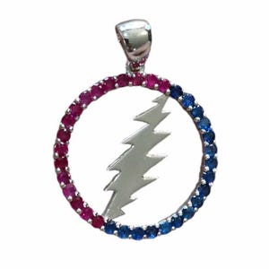 May include: Silver pendant with a lightning bolt design inside a circle, adorned with alternating pink and blue gemstones. The pendant has a silver bail for a chain. The gemstones are in a circular pattern.