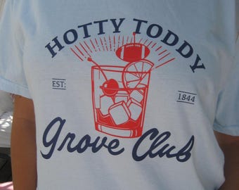 May include: A white t-shirt with a blue and red graphic design. The graphic features a glass of ice with a cherry and a football, with the text "Hotty Toddy Grove Club Est: 1844".