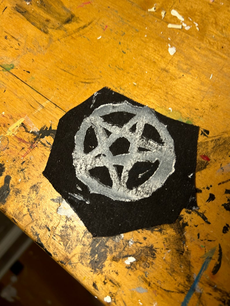 Puede incluir: Un parche de tela negro con un dise&ntilde;o de pentagrama blanco. El parche est&aacute; sobre una superficie de madera.