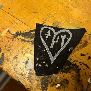 May include: A black fabric heart-shaped patch with white paint outlining the heart and the word "H.U.Y." written inside.