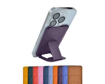 May include: A purple leather phone stand with a kickstand for propping up a smartphone. The stand is attached to the back of a silver smartphone with a camera lens.