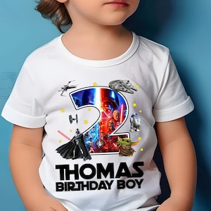 May include: White t-shirt with a colourful Star Wars themed design featuring a number 2, characters, and spaceships. The text "THOMAS BIRTHDAY BOY" is printed on the shirt.