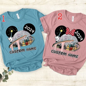 Puede incluir: Dos camisetas con un dise&ntilde;o de orejas de Mickey Mouse que presenta un gr&aacute;fico de Spaceship Earth y el texto "2024" y "CUSTOM NAME". La camiseta de la izquierda es azul y la camiseta de la derecha es rosa.