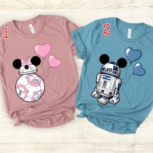 Puede incluir: Dos camisetas con temática de Star Wars. La primera camiseta es rosa con un droide BB-8 blanco y rosa que lleva orejas de Minnie Mouse y sostiene globos rosas. La segunda camiseta es azul con un droide R2-D2 blanco que lleva orejas de Mickey Mouse y sostiene globos azules. Las camisetas están numeradas 1 y 2.
