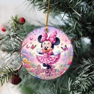 May include: A round Christmas ornament featuring Minnie Mouse in a pink polka-dot dress and bow. The ornament has a floral and butterfly background with the name "Jessie" and the year "2025" printed on it.