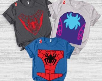 Puede incluir: Tres camisetas con diseños de superhéroes. Una es gris oscuro con un emblema de araña roja, otra es gris claro con un diseño de araña azul y la tercera es azul con un emblema de araña roja y negra.