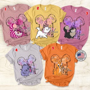 Puede incluir: Cinco camisetas diferentes con una cabeza de rat&oacute;n de dibujos animados con un castillo y fuegos artificiales en el fondo. Cada camiseta presenta un personaje diferente de Disney: Marie, Figaro, Duquesa, Berlioz y Toulouse. Las camisetas son de varios colores, incluyendo rosa, amarillo, gris y naranja.