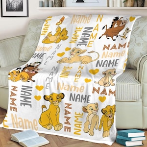 May include: White fleece blanket featuring illustrations of characters from The Lion King, including Simba, Timon, Pumbaa, and Nala. The blanket has the word "Name" printed in various fonts and colors, along with yellow hearts.