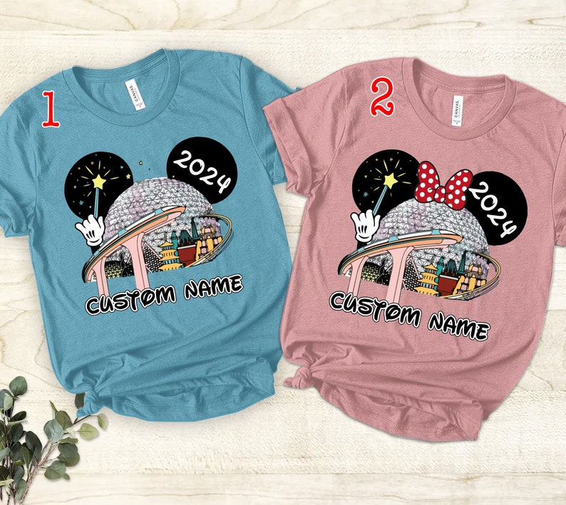 Puede incluir: Dos camisetas con un dise&ntilde;o de orejas de Mickey Mouse que presenta un gr&aacute;fico de Spaceship Earth y el texto "2024" y "CUSTOM NAME". La camiseta de la izquierda es azul y la camiseta de la derecha es rosa.