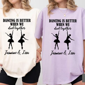 Peut inclure: Deux t-shirts avec le texte "Dancing is better when we duet together" et les noms "Jasmine & Lisa". Les t-shirts sont de couleur ivoire et orchidée. Le design présente deux silhouettes de ballerines.