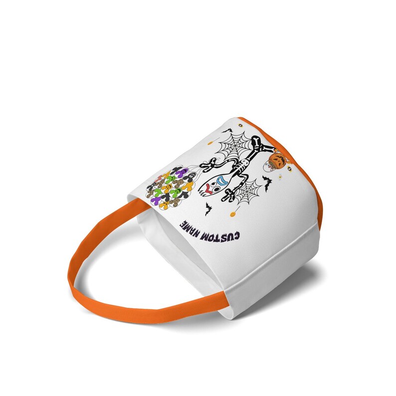 Op de afbeelding: Witte Halloween-draagtas met een oranje handvat. De tas heeft een skelet op een bezem, spinnenwebben en een pompoenontwerp. De tekst "CUSTOM NAME" staat op de zijkant van de tas.