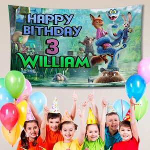 May include: A birthday banner with the text "HAPPY BIRTHDAY 3 WILLIAM" in blue, pink, and green. The banner features cartoon characters and a river scene. Colorful balloons and children wearing party hats are in the foreground.