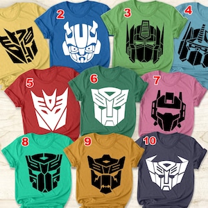 Può includere: Dieci magliette diverse con vari loghi dei Transformers stampati su di esse. Le magliette sono di diversi colori, tra cui giallo, blu, verde, rosso, rosa, verde acqua, oro e blu navy.