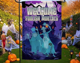 Op de afbeelding: Een rechthoekige tuin vlag met een paarse en zwarte achtergrond van een spookhuis met de tekst WELCOME FOOLISH MORTALS in het wit. Drie lichtblauwe cartoongeesten met hoge hoeden en formele kleding staan op de voorgrond.