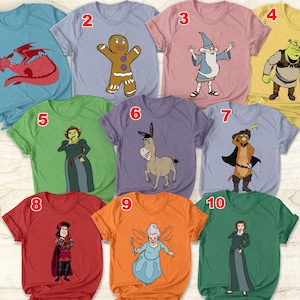 Könnte beinhalten: Eine Sammlung von zehn kurzärmeligen T-Shirts, die jeweils eine andere Zeichentrickfigur aus dem Animationsfilm Shrek zeigen. Die Shirts sind in verschiedenen Farben erhältlich, darunter Blau, Rosa, Grün, Gelb, Lila, Orange und Rot.