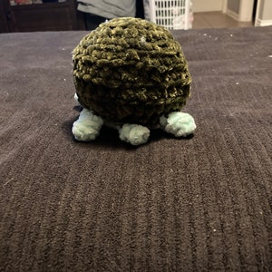 May include: A green crocheted octopus with light blue tentacles. The octopus is sitting on a dark gray surface.