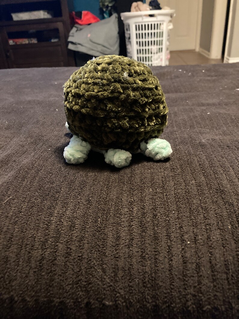 May include: A green crocheted octopus with light blue tentacles. The octopus is sitting on a dark gray surface.