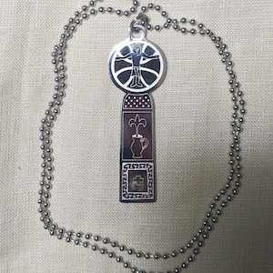 May include: A silver necklace with a pendant featuring a stylized human figure, a vase with a flower, and a cross. The pendant is attached to a silver ball chain.