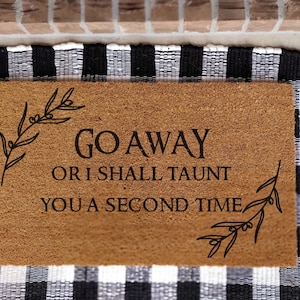 May include: A brown coir doormat with the text "GO AWAY OR I SHALL TAUNT YOU A SECOND TIME" in black lettering. The doormat has a black and white checkered background.