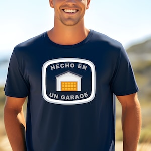 May include: Navy blue t-shirt with a white and yellow garage graphic and the text "HECHO EN UN GARAGE". The graphic is in a white square with rounded corners. The shirt is a crew neck.