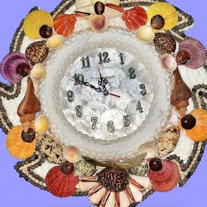 Puede incluir: Un reloj de pared decorativo con una esfera blanca y números y manecillas negras. El reloj está adornado con una variedad de conchas marinas coloridas en tonos naranja, amarillo, rojo y morado, creando un tema costero único.