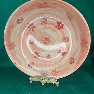 May include: A large, round ceramic bowl featuring a hand-painted, swirled peach and cream-colored glaze. The interior surface is decorated with a repeating pattern of small, dark orange floral motifs scattered across the base and sides.