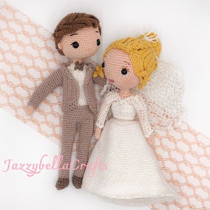 Puede incluir: Muñecas de crochet de novia y novio. La novia lleva un vestido blanco con velo y tiene el pelo rubio. El novio lleva un traje marrón con camisa blanca y pajarita. Las muñecas están de pie sobre un fondo de color melocotón.