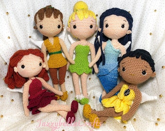 May include: Six crocheted dolls with wings, each wearing a different colored dress. The dolls have brown, blonde, and black hair, and one doll has brown skin. The dolls are sitting on a white background with gold glitter.