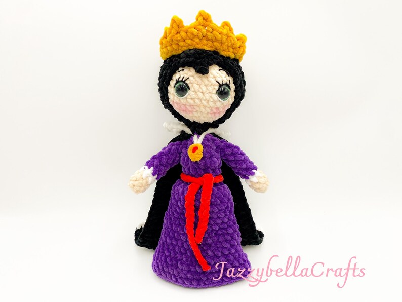 Pode incluir: Boneca de croch&ecirc; feita &agrave; m&atilde;o de uma rainha, com capa preta, vestido roxo e coroa de ouro. A boneca tem um cinto vermelho e um pingente de ouro. &Eacute; um item artesanal caprichoso.