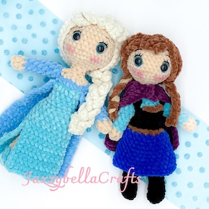 May include: Two crocheted dolls dressed as Elsa and Anna from the movie Frozen. Elsa is wearing a light blue dress with a white braid and Anna is wearing a purple cape and a blue dress.