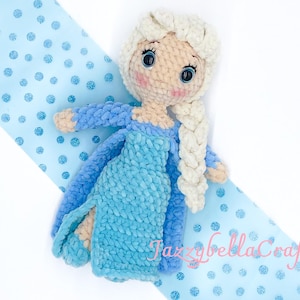 May include: Crocheted doll with a blue dress and white braid, against a blue background with white polka dots. The doll has a light skin tone, blue eyes, and pink cheeks.