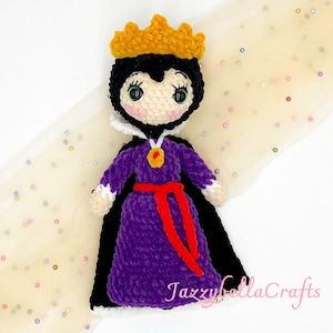 May include: Crocheted doll of a queen wearing a gold crown, black cape, and purple dress with a red belt. The doll has a white collar and a gold pendant. The doll's face is white with black hair and green eyes.