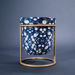 May include: A white ceramic mug with a black handle and the text "But First, Coffee" in a bold, black font. The mug is set against a blurred background, suggesting a cosy setting.