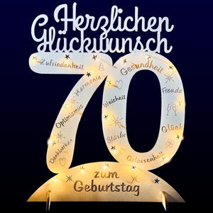 May include: A wooden 70th birthday sign with lights and the words "Herzlichen Glückwunsch" and "zum Geburtstag". The sign is decorated with words like "Zufriedenheit", "Harmonie", "Optimismus", "Dankbarkeit", "Weisheit", "Gesundheit", "Stärke", "Gelassenheit", "Freude", and "Glück".