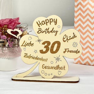May include: A wooden clover-shaped sign with the words "Happy Birthday 30" and the words "Liebe, Zufriedenheit, Gesundheit, Gl&uuml;ck, Freude" in a gold colour.