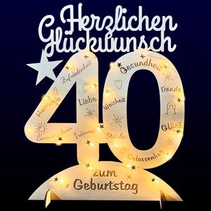 May include: A wooden 40th birthday sign with a star and lights. The sign has the words "Herzlichen Glückwunsch" and "zum Geburtstag" on it. The number 40 is surrounded by words like "Liebe", "Freude", and "Glück".