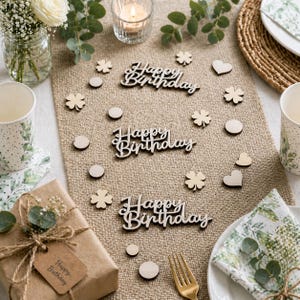 May include: A festive birthday table setting with a burlap runner. Wooden cutouts include "Happy Birthday" script, clovers, circles, and hearts. A wrapped gift, floral napkin, and gold fork complete the scene. A lit candle and floral arrangement add to the decor.
