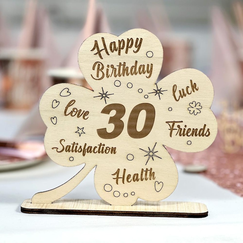 May include: Wooden clover-shaped sign with the text "Happy Birthday 30" and the words "love, satisfaction, health, luck, friends" around the number 30.