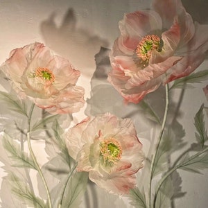 Puede incluir: Tres delicadas flores de papel de color rosa p&aacute;lido con centros verdes. Las flores est&aacute;n dispuestas en tallos con hojas verdes sobre un fondo blanco.