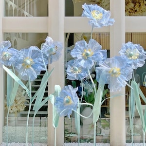 Puede incluir: Primer plano de un ramo de flores de papel azul claro. Las flores est&aacute;n dispuestas en un jarr&oacute;n y est&aacute;n enfocadas, mientras que el fondo est&aacute; desenfocado.