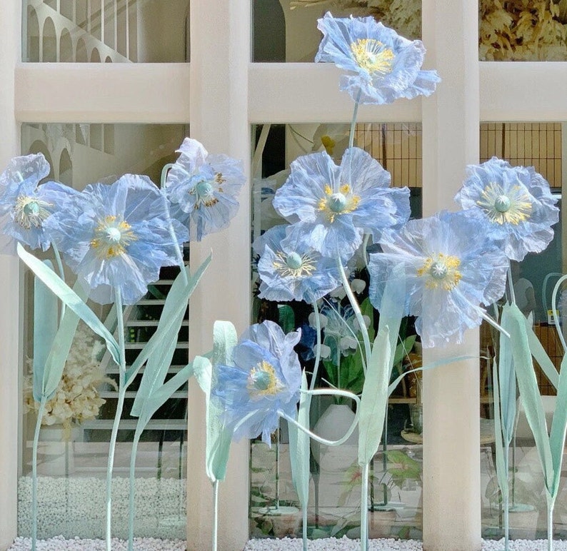 Puede incluir: Primer plano de un ramo de flores de papel azul claro. Las flores est&aacute;n dispuestas en un jarr&oacute;n y est&aacute;n enfocadas, mientras que el fondo est&aacute; desenfocado.