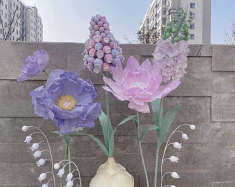 Puede incluir: Un ramo de flores de papel en tonos de rosa, morado y blanco. Las flores están dispuestas en un jarrón e incluyen una flor rosa grande, una flor morada y un grupo de flores blancas.