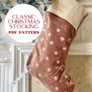May include: A brown velvet Christmas stocking with a white snowflake pattern and a beige cuff. The stocking is hanging on a white fireplace mantel. The text "CLASSIC CHRISTMAS STOCKING PDF PATTERN" is written in red on a white circle.
