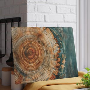 May include: A square wooden cutting board with a natural wood grain pattern. The center features concentric rings of brown and tan, transitioning to a teal-colored edge. The board is displayed near a window and kitchen utensils.